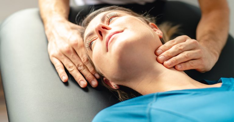Φυσικοθεραπευτής εφαρμόζει χειροθεραπεία στον αυχένα ξαπλωμένης γυναίκας, σε περίπτωση μουδιάσματος στο χέρι