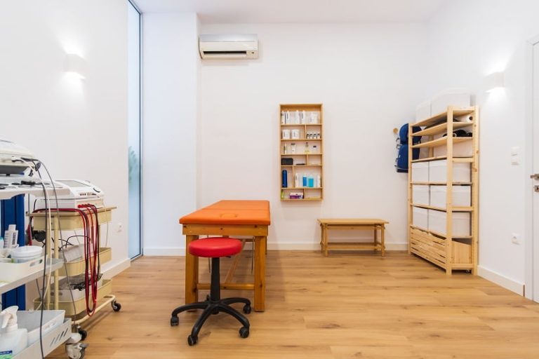 Εσωτερικός χώρος κλινικής με ιατρικό εξοπλισμό, κρεβάτι εξετάσεων, και ξύλινα έπιπλα.